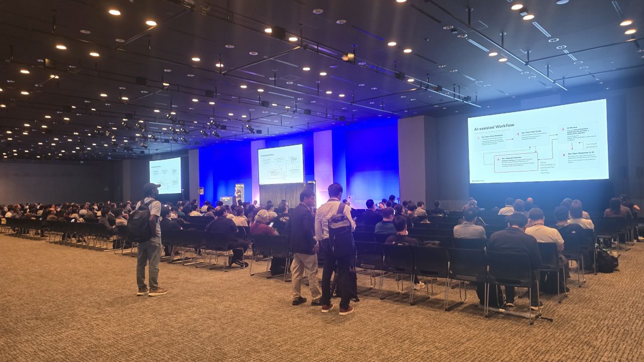 A large conference hall at AGNTCon + MCPCon Japan 2026 in Tokyo, with rows of attendees facing a stage and three screens
